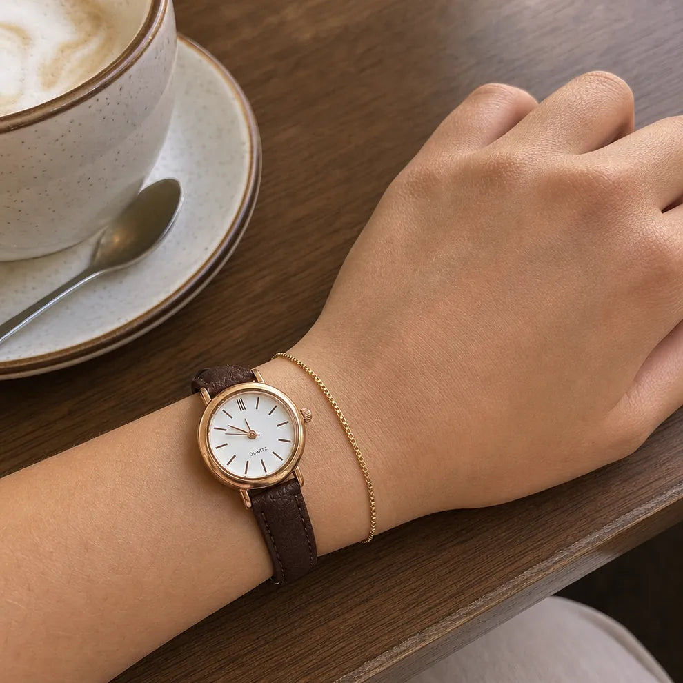 Reloj con caja en tono oro rosa y pulso de cuero café junto a la pulsera fina en la muñeca